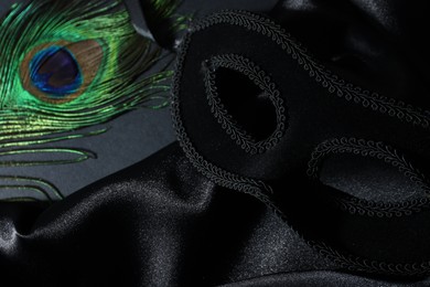 Photo of Beautiful carnival mask, peacock feather and fabric on black background, closeup