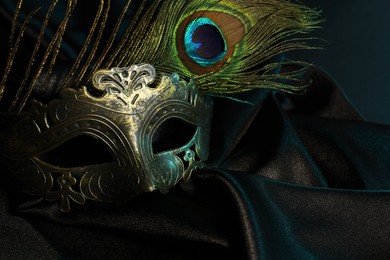 Photo of Beautiful carnival mask and peacock feather on black fabric, closeup