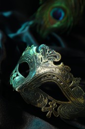 Beautiful carnival mask and peacock feather on black fabric, closeup