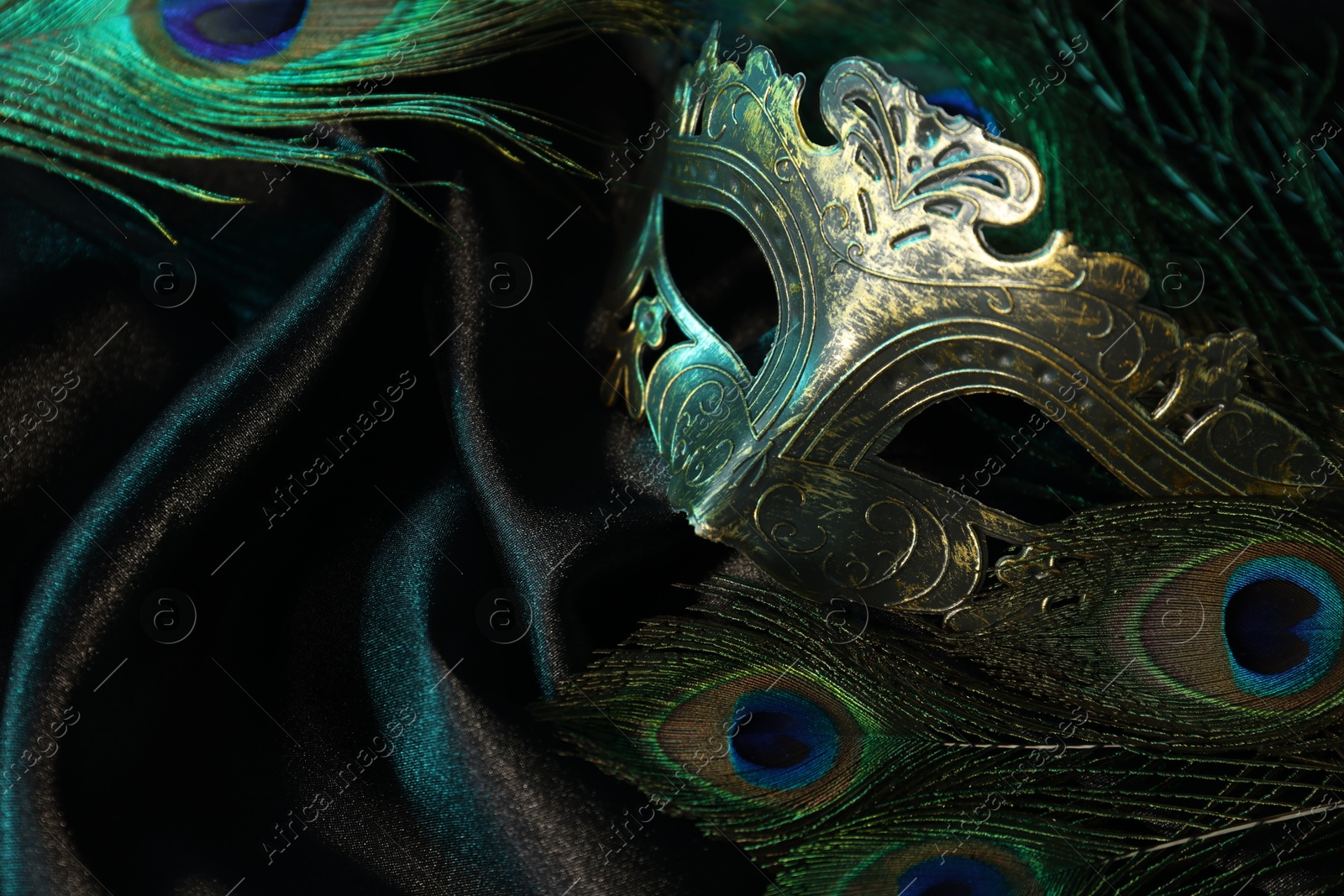 Photo of Beautiful carnival mask and peacock feathers on black fabric, closeup