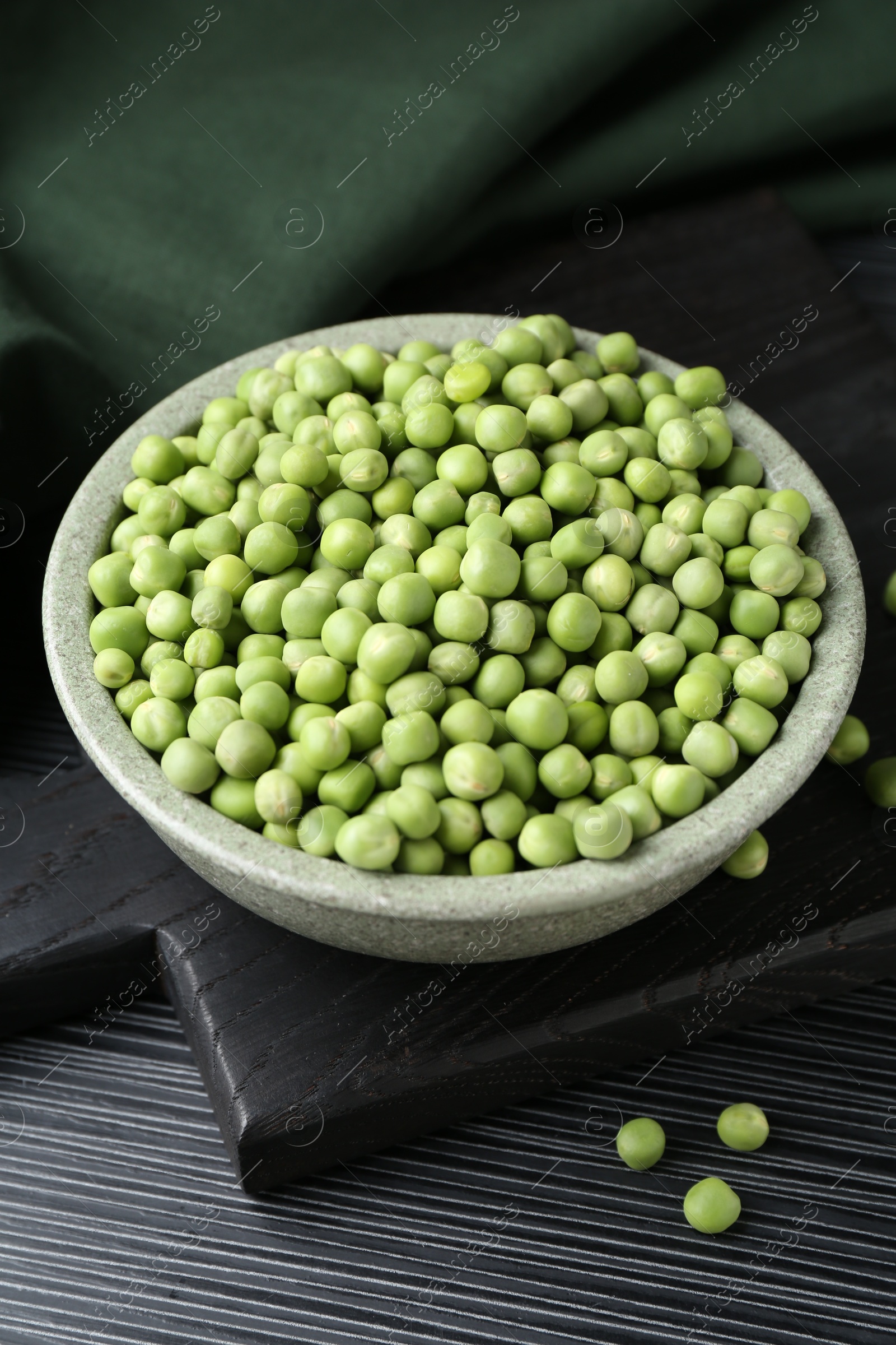 Photo of Fresh green peas in bowl on black wooden table, closeup