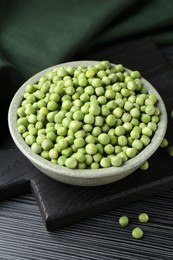 Fresh green peas in bowl on black wooden table, closeup