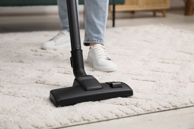 Photo of Woman cleaning carpet with vacuum indoors, closeup