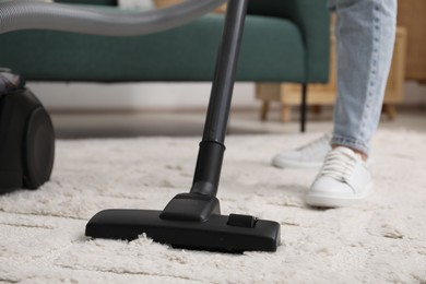 Photo of Woman cleaning carpet with vacuum indoors, closeup