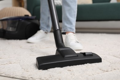 Photo of Woman cleaning carpet with vacuum indoors, closeup