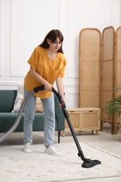 Photo of Young woman cleaning carpet with vacuum in living room