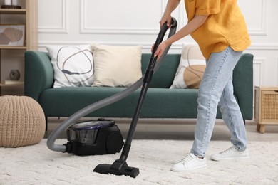 Photo of Woman cleaning carpet with vacuum in living room, closeup