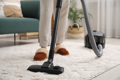 Photo of Woman cleaning carpet with vacuum in living room, closeup