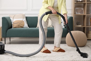 Photo of Woman cleaning carpet with vacuum in living room, closeup