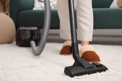 Woman cleaning carpet with vacuum indoors, closeup