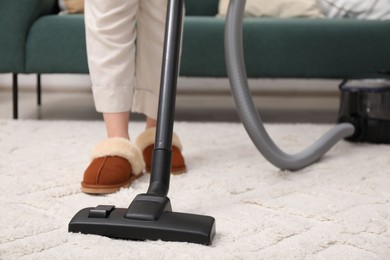 Photo of Woman cleaning carpet with vacuum indoors, closeup