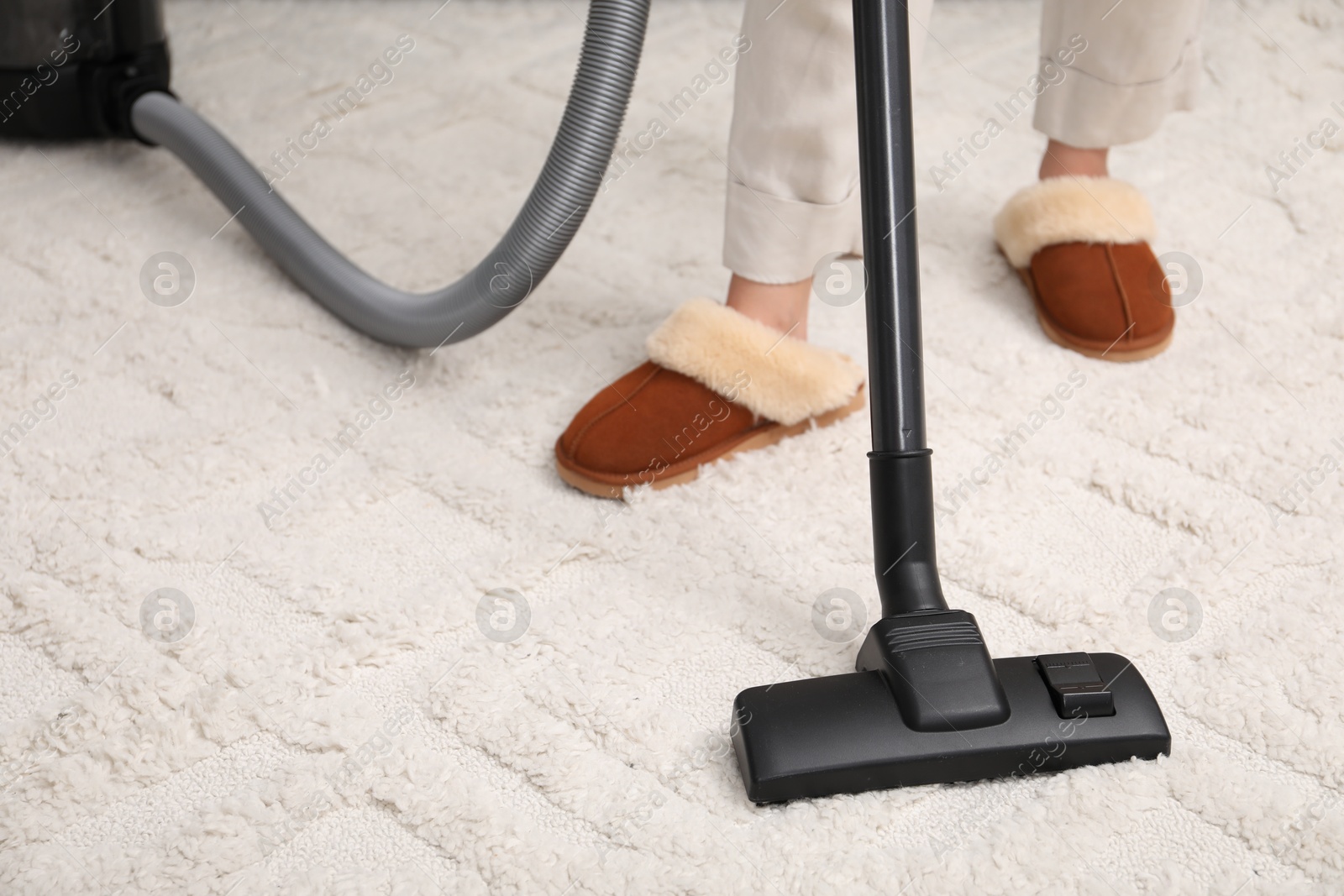 Photo of Woman cleaning carpet with vacuum indoors, closeup