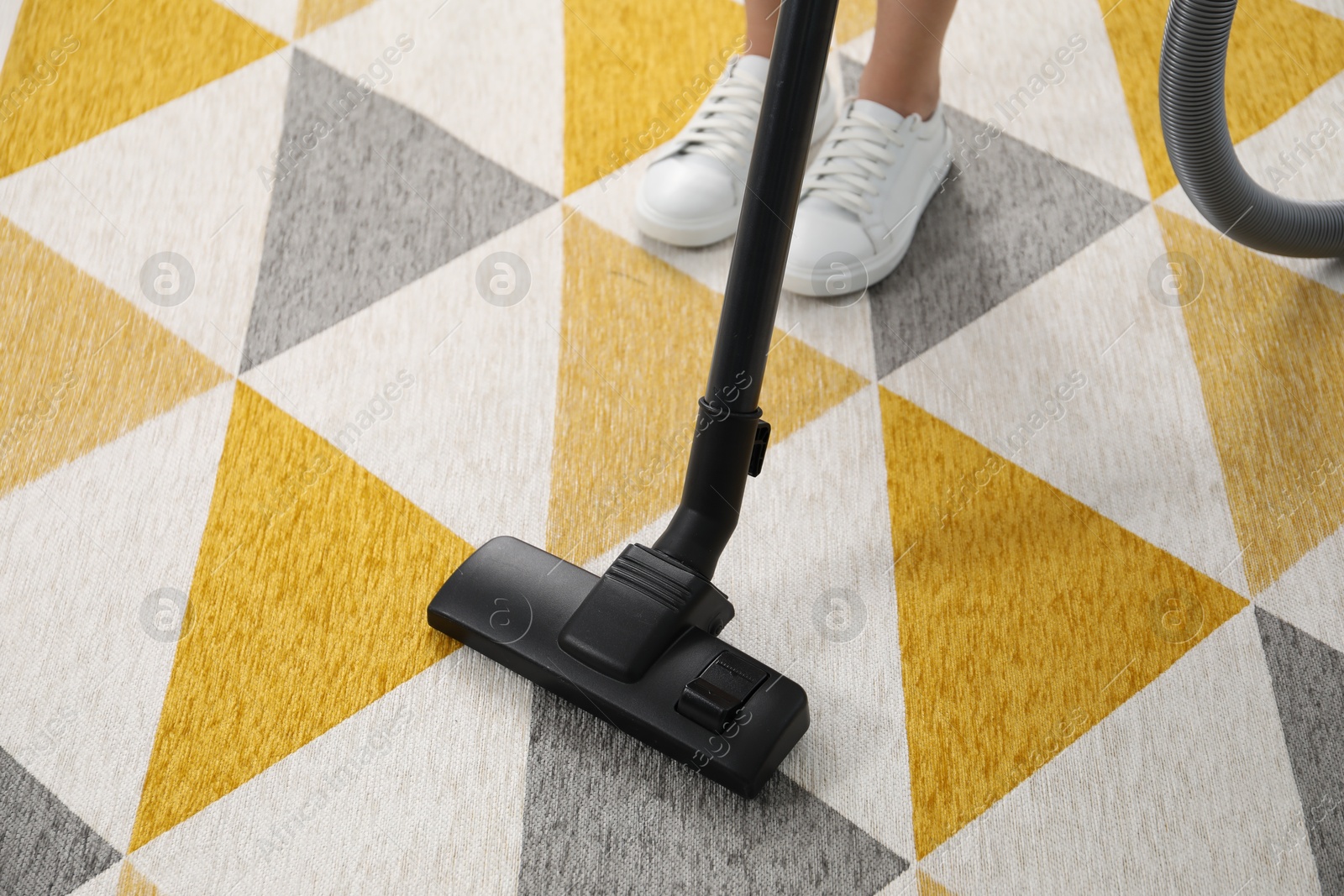 Photo of Woman vacuuming bright carpet indoors, closeup view