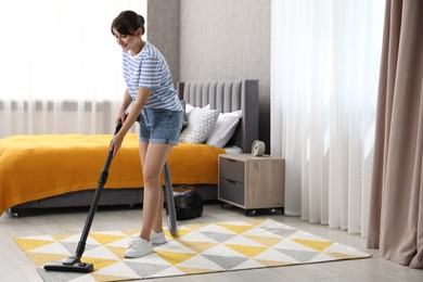 Photo of Young woman cleaning carpet with vacuum in bedroom