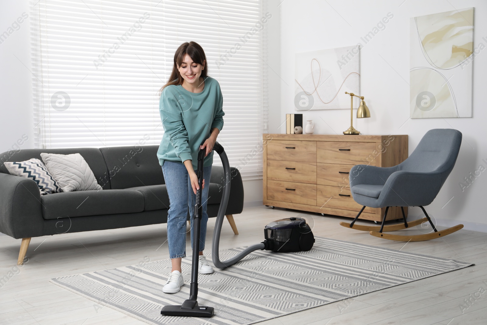 Photo of Young woman vacuuming carpet in living room