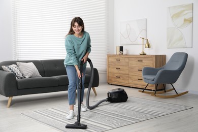 Photo of Young woman vacuuming carpet in living room