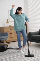 Photo of Young woman in headphones having fun while vacuuming carpet at home