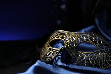 Beautiful carnival mask on blue fabric in darkness, closeup