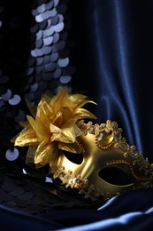 Photo of Beautiful golden carnival mask on blue fabric in darkness