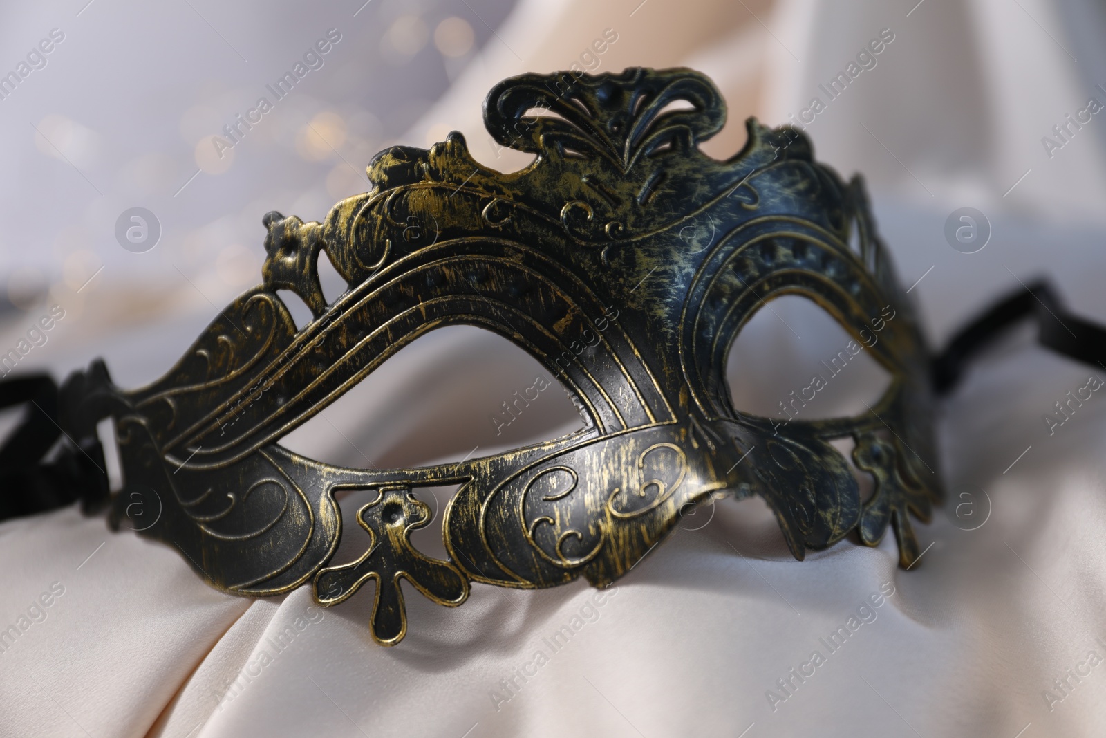 Photo of Beautiful carnival mask on light silk fabric , closeup