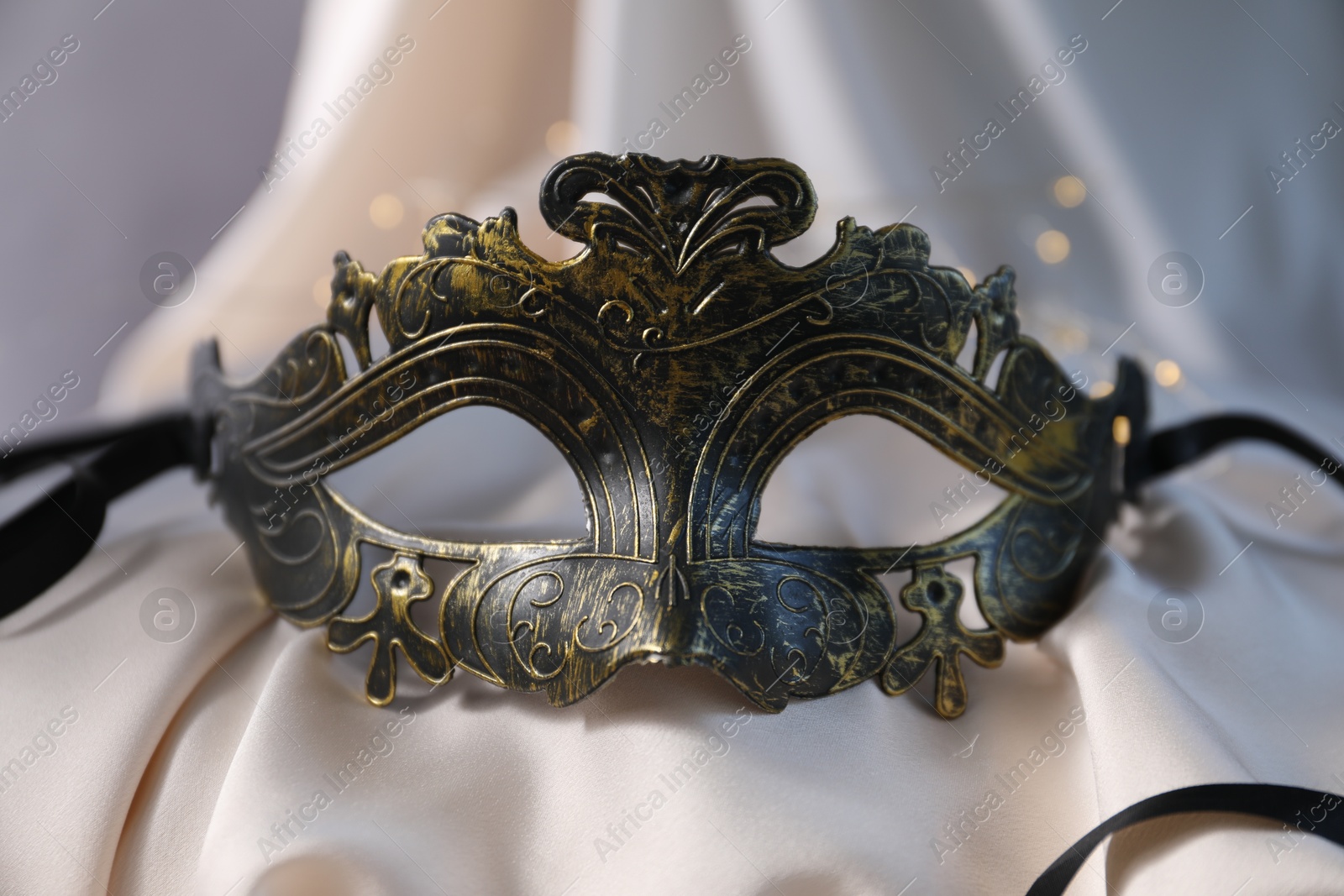 Photo of Beautiful carnival mask on light silk fabric , closeup