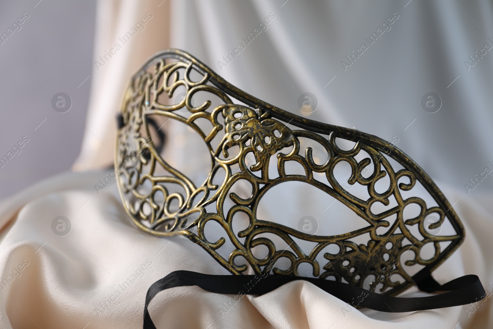 Photo of Beautiful carnival mask on light silk fabric , closeup