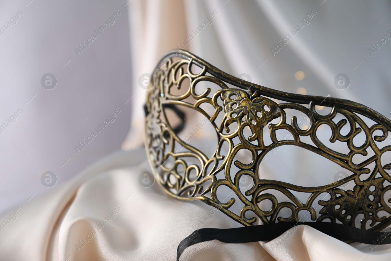 Photo of Beautiful carnival mask on light silk fabric , closeup