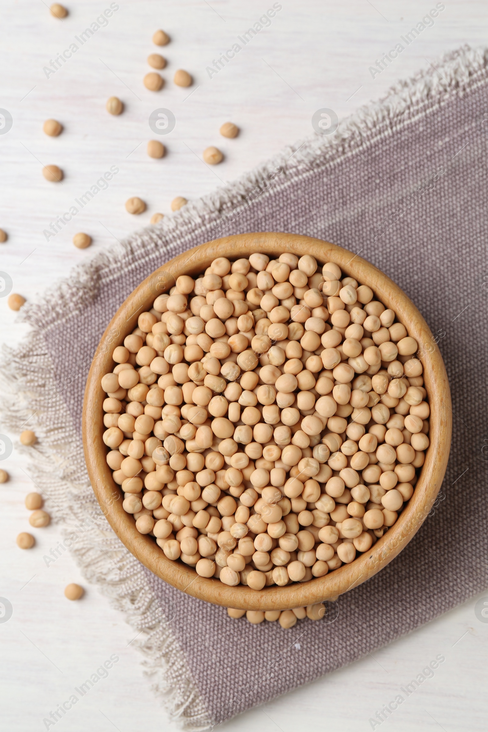 Photo of Dried peas in bowl on light wooden table, top view