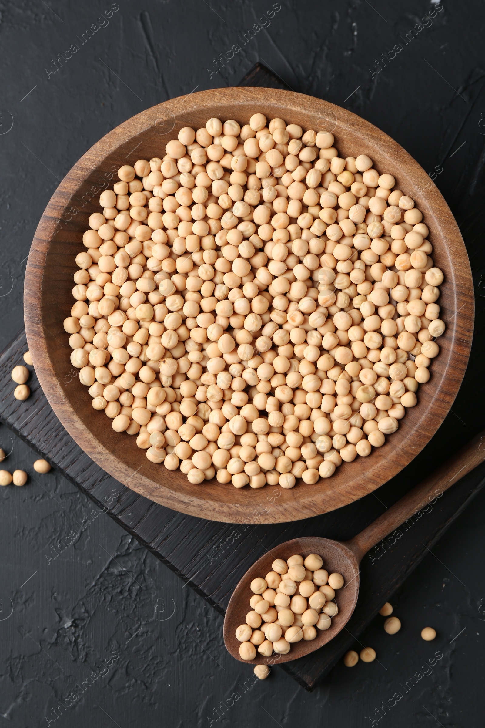 Photo of Dried peas in bowl and spoon on dark textured table, top view