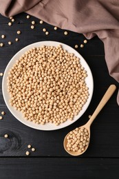 Photo of Dried peas in bowl and spoon on black wooden table, flat lay