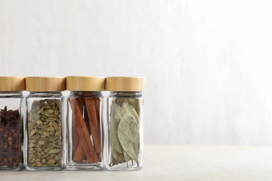 Different spices in glass jars on light textured table, closeup. Space for text