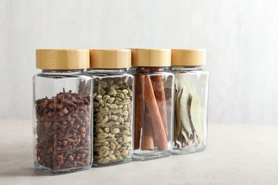 Different spices in glass jars on light table, closeup