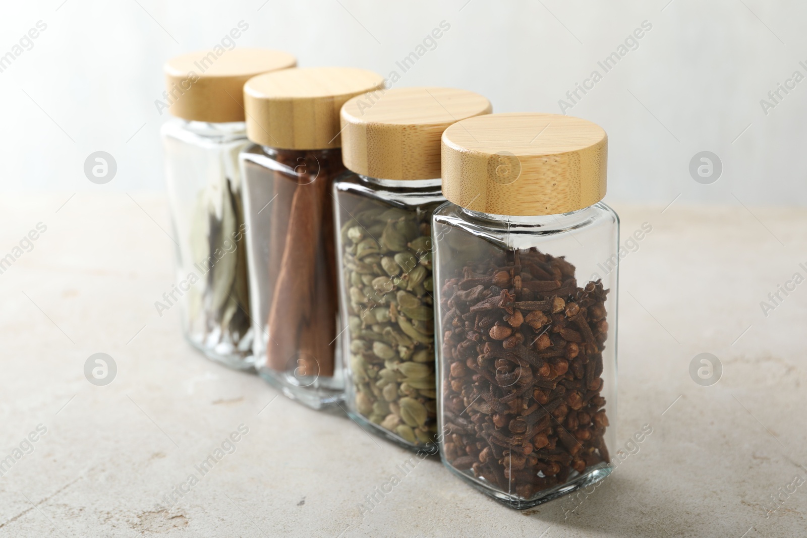 Photo of Different spices in glass jars on light textured table, closeup