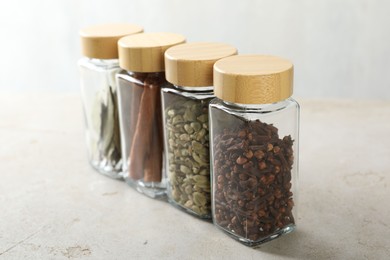 Photo of Different spices in glass jars on light textured table, closeup