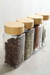 Different spices in glass jars on light textured table, closeup