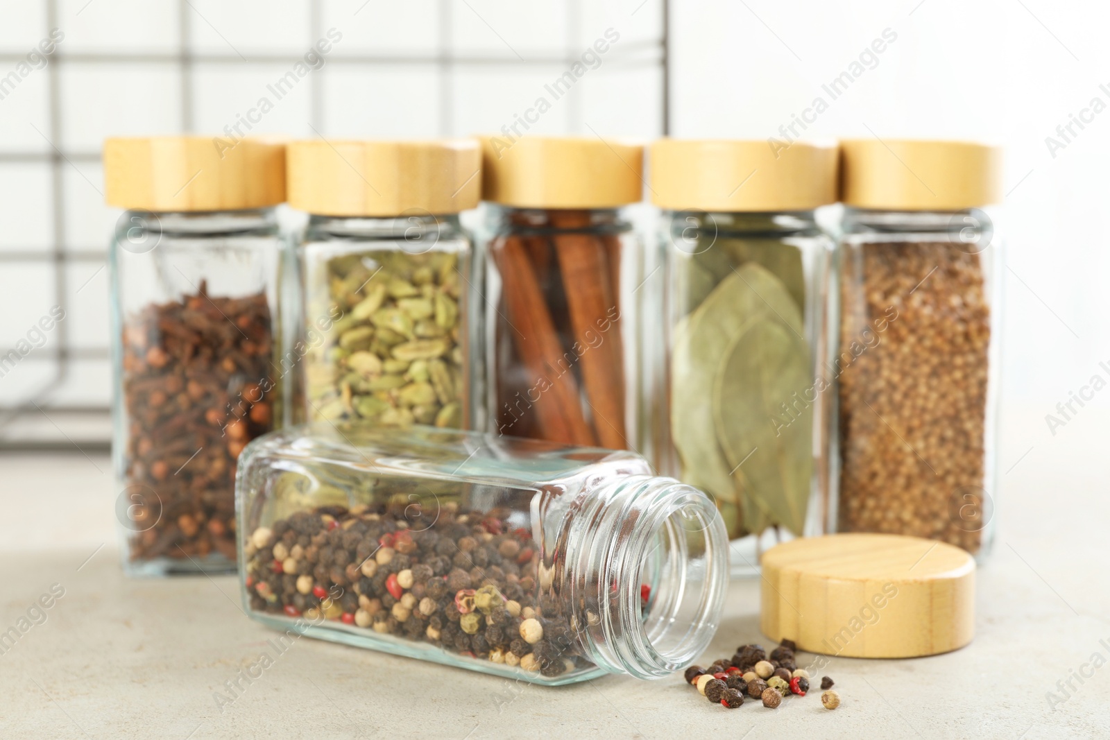 Photo of Different spices in glass jars on light textured table, closeup