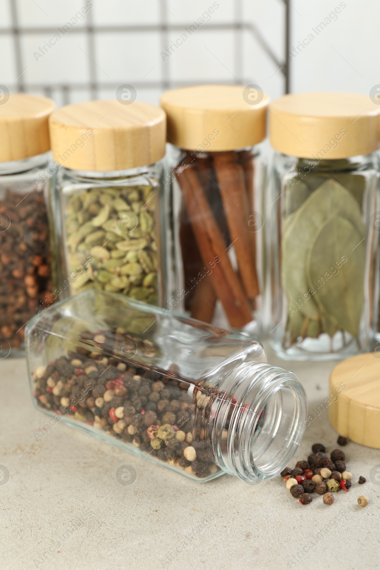 Photo of Different spices in glass jars on light textured table, closeup