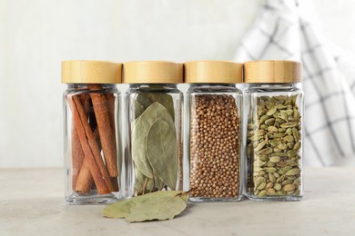 Photo of Different spices in glass jars on light textured table, closeup