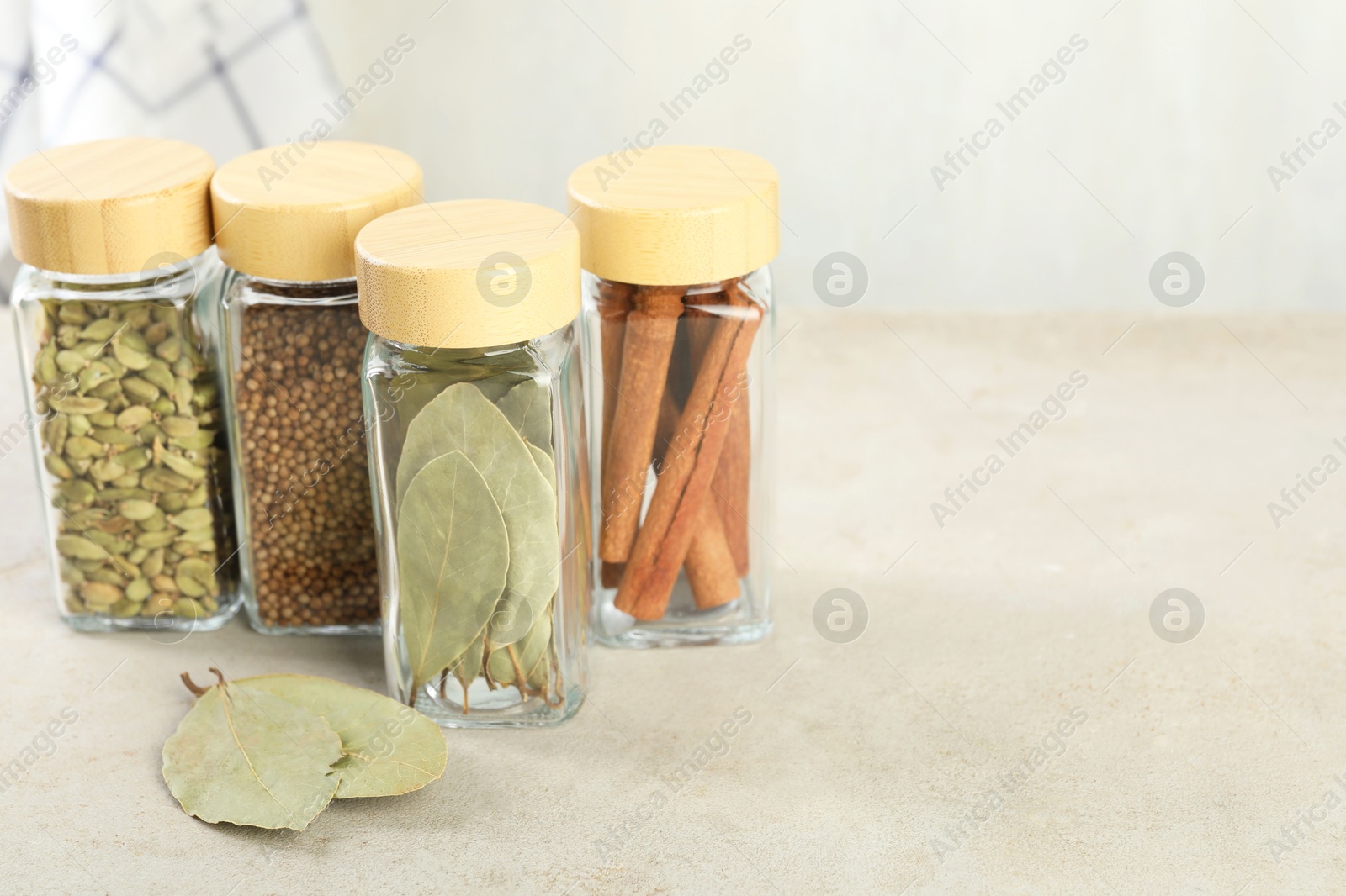 Photo of Different spices in glass jars on light textured table. Space for text