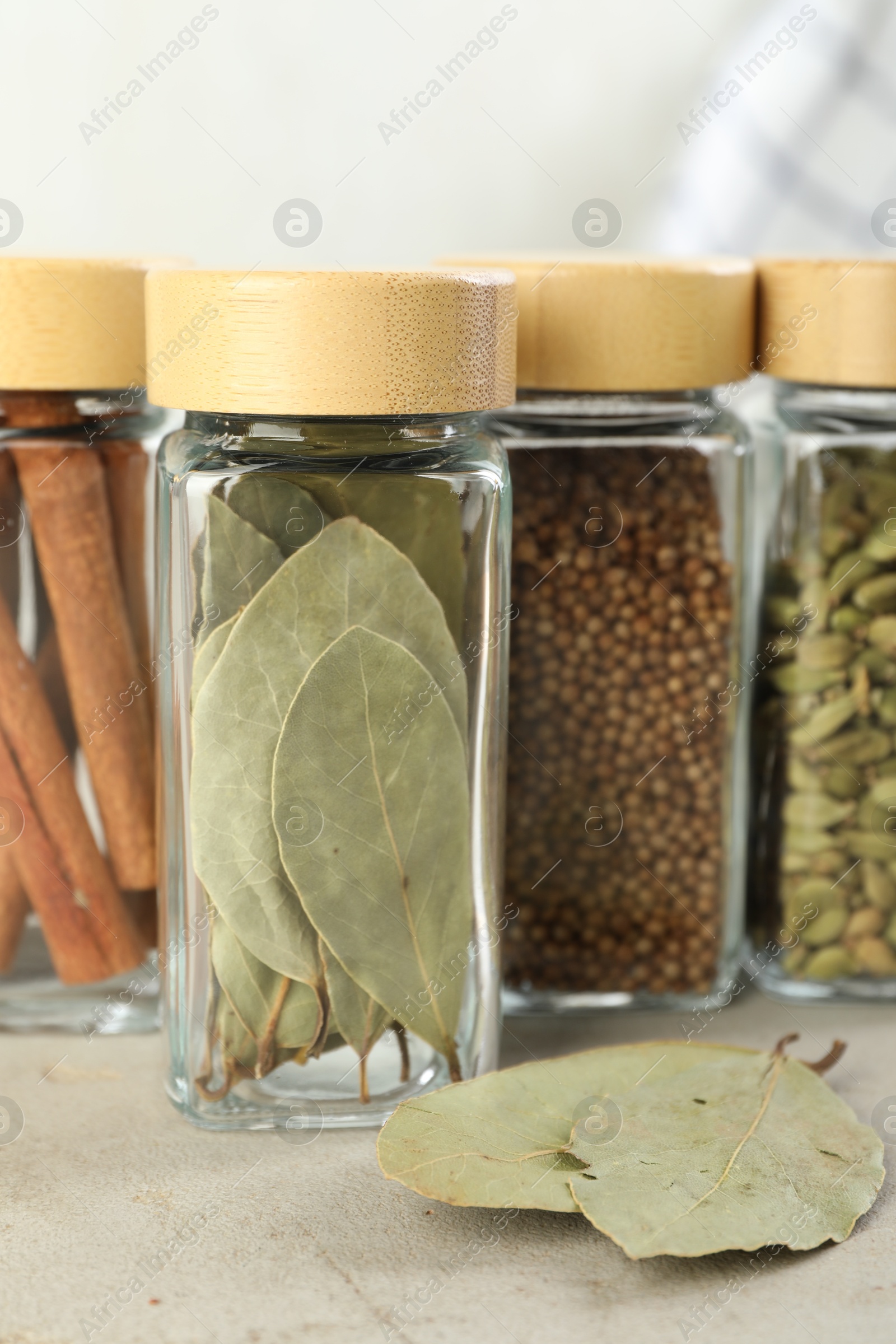 Photo of Different spices in glass jars on light textured table, closeup