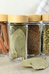 Photo of Different spices in glass jars on light textured table, closeup