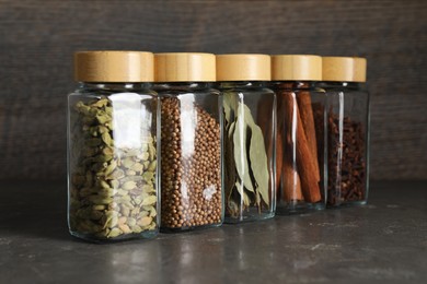 Different spices in glass jars on dark textured table, closeup