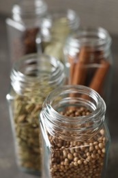 Photo of Different spices in glass jars on blurred background, closeup