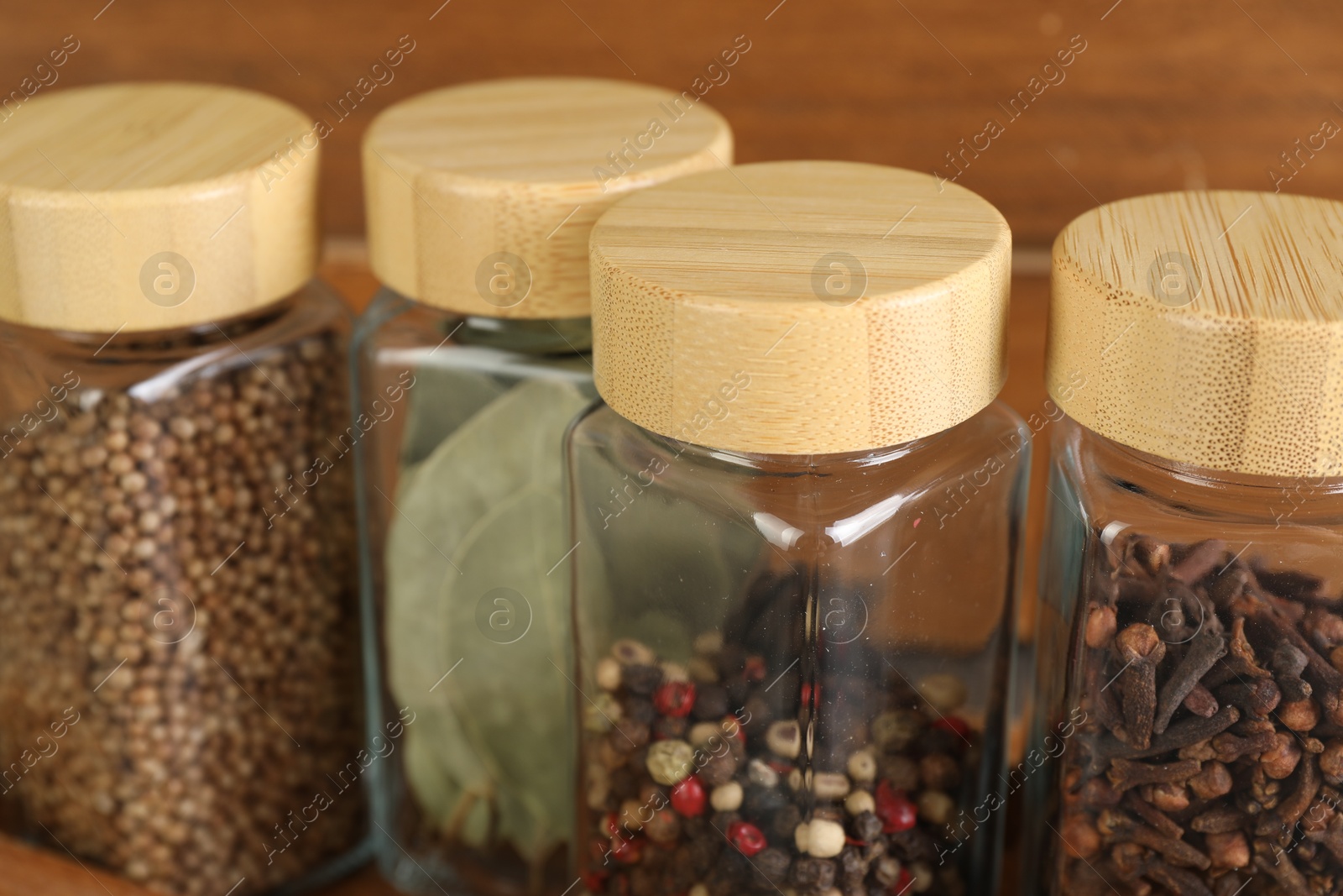 Photo of Different spices in glass jars on blurred background, closeup