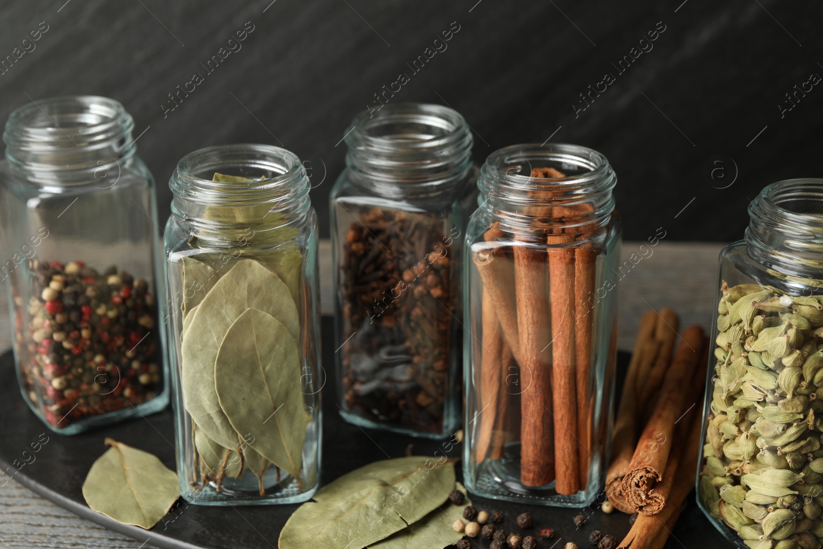 Photo of Different spices in glass jars on grey wooden table, closeup