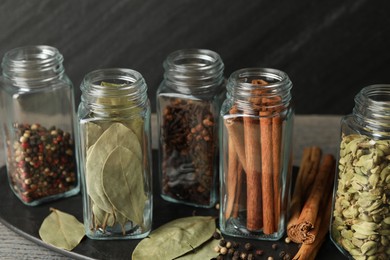 Different spices in glass jars on grey wooden table, closeup