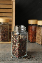 Photo of Peppercorns in glass jar and other spices on grey wooden table, closeup