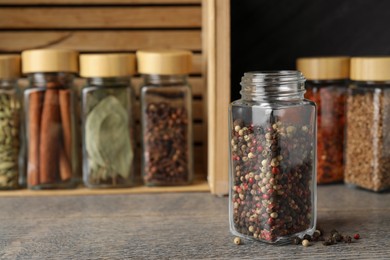 Peppercorns in glass jar and other spices on grey wooden table, closeup