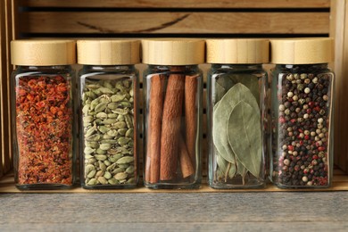 Photo of Different spices in glass jars on grey wooden table, closeup