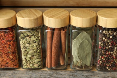 Photo of Different spices in glass jars on grey wooden table, closeup